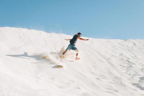 Sandboarding in Lancelin, Western Australia, with a traveller riding down the famous white dunes during an exciting outdoor adventure experience.